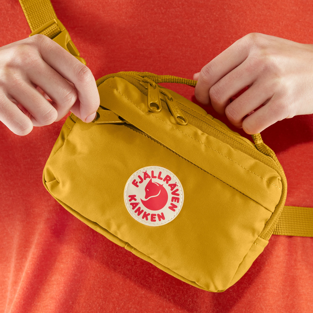 Kånken Hip Pack in yellow being worn, featuring a durable Vinylon F fabric, adjustable strap, and multiple zippered pockets.