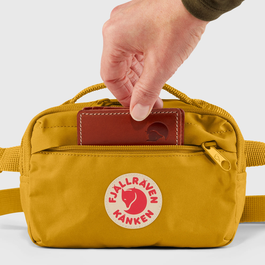 Kånken Hip Pack in yellow with a red logo, featuring durable Vinylon F fabric, main compartment, and adjustable strap.