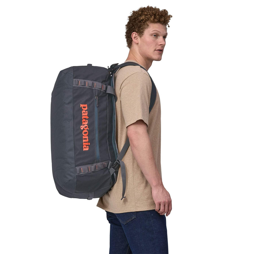 Man carrying Black Hole Duffel 55L as backpack, showing ergonomic design and robust material.