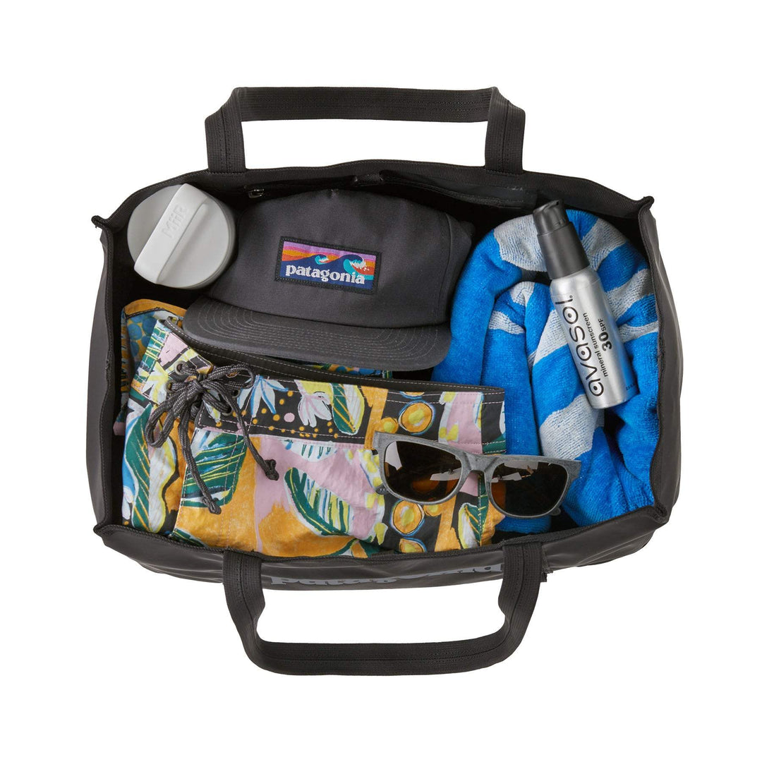 Black Hole Tote 25L filled with gear, featuring durable and lightweight recycled polyester, two organizational pockets, and convenient handles.