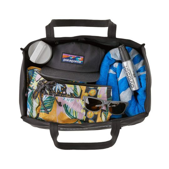 Black Hole Tote 25L filled with gear, featuring durable and lightweight recycled polyester, two organizational pockets, and convenient handles.