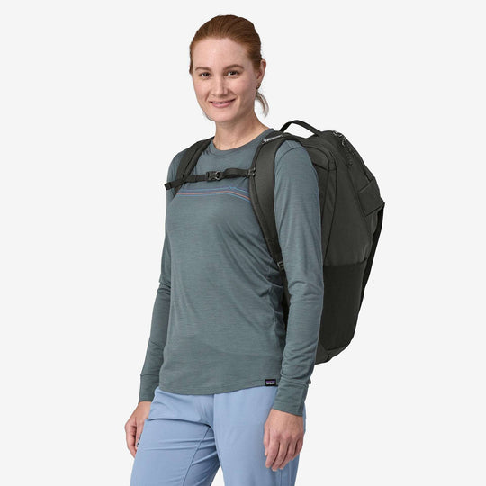 Woman wearing Black Hole Pack 32L backpack, made from recycled polyester with water-repellent finish.