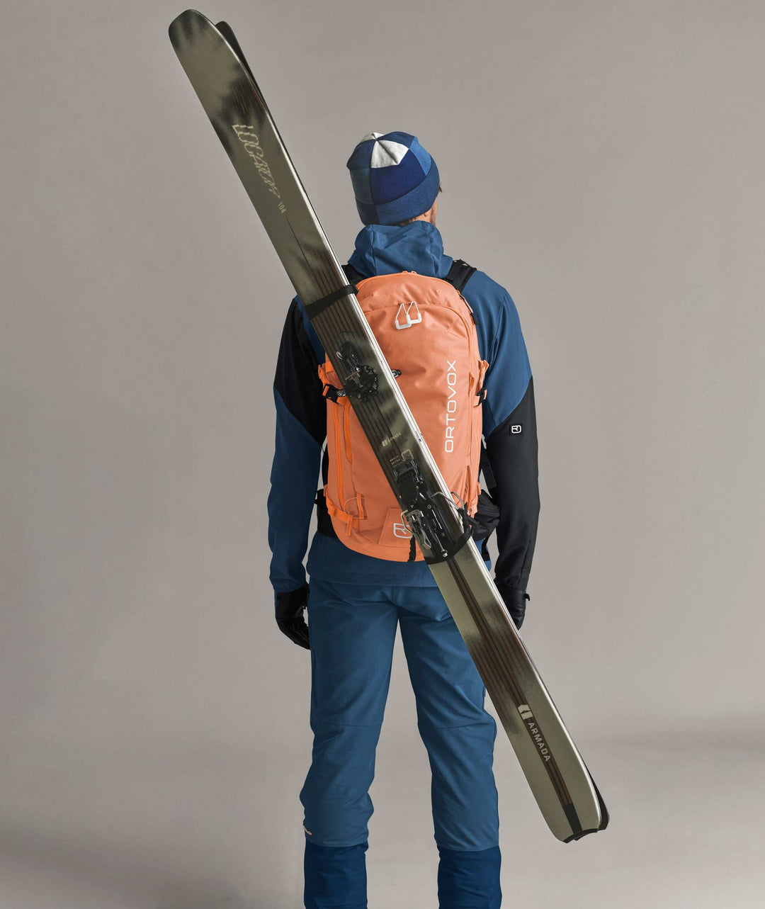 Ortovox Venet Tour 30 Faded Tangerine, indossato con sci fissati in diagonale