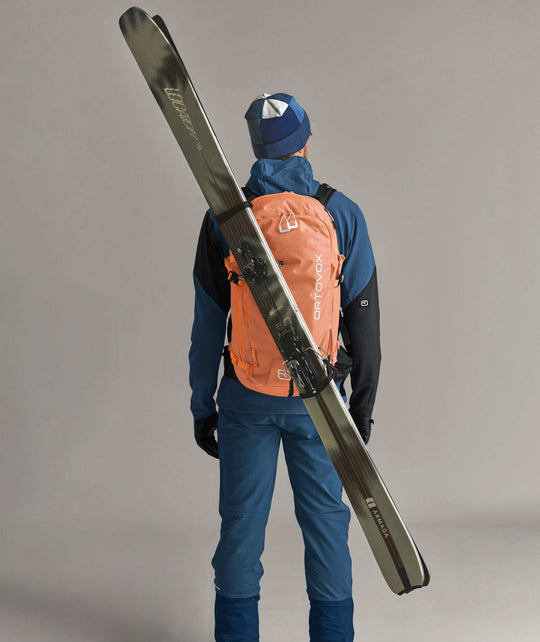 Ortovox Venet Tour 30 Faded Tangerine, indossato con sci fissati in diagonale