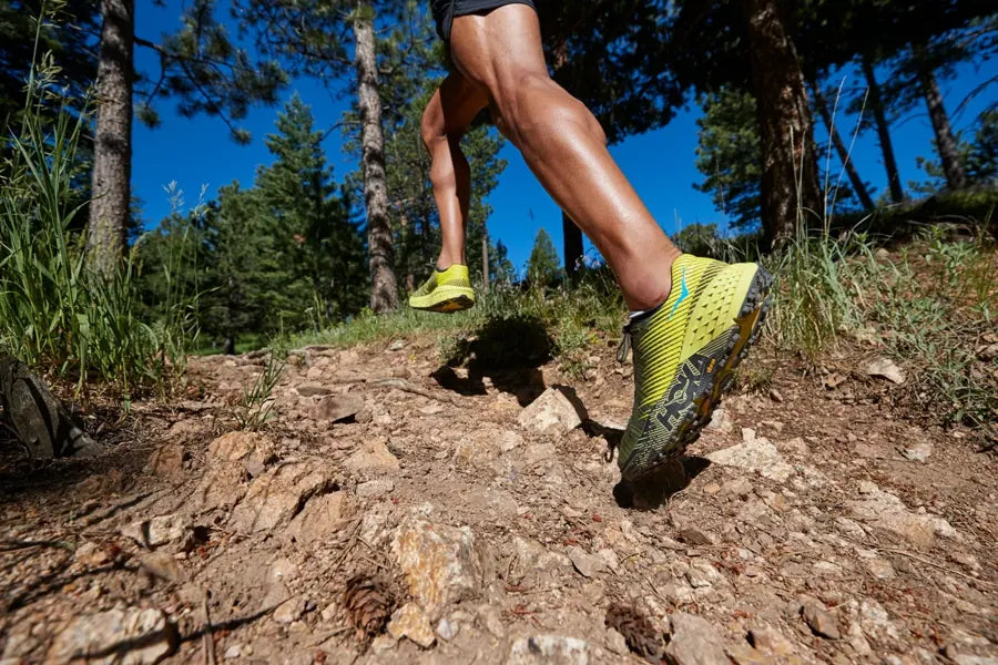 A runner wearing HOKA shoes on a forest trail
